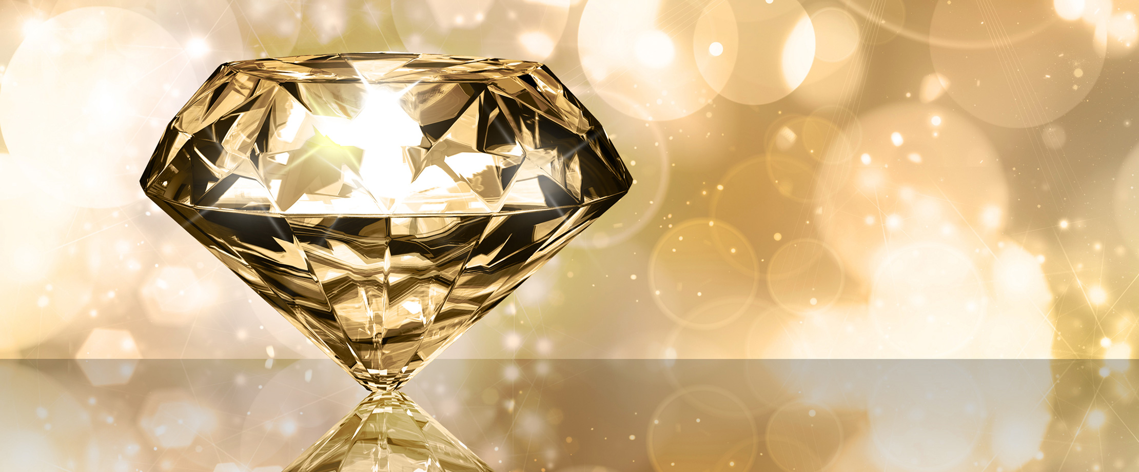 Diamanten & Brillanten Ein Brillant liegt auf einem Tisch. Der Hintergrund ist gelb beleuchtet, weswegen der Diamant golden zu leuchten scheint.
